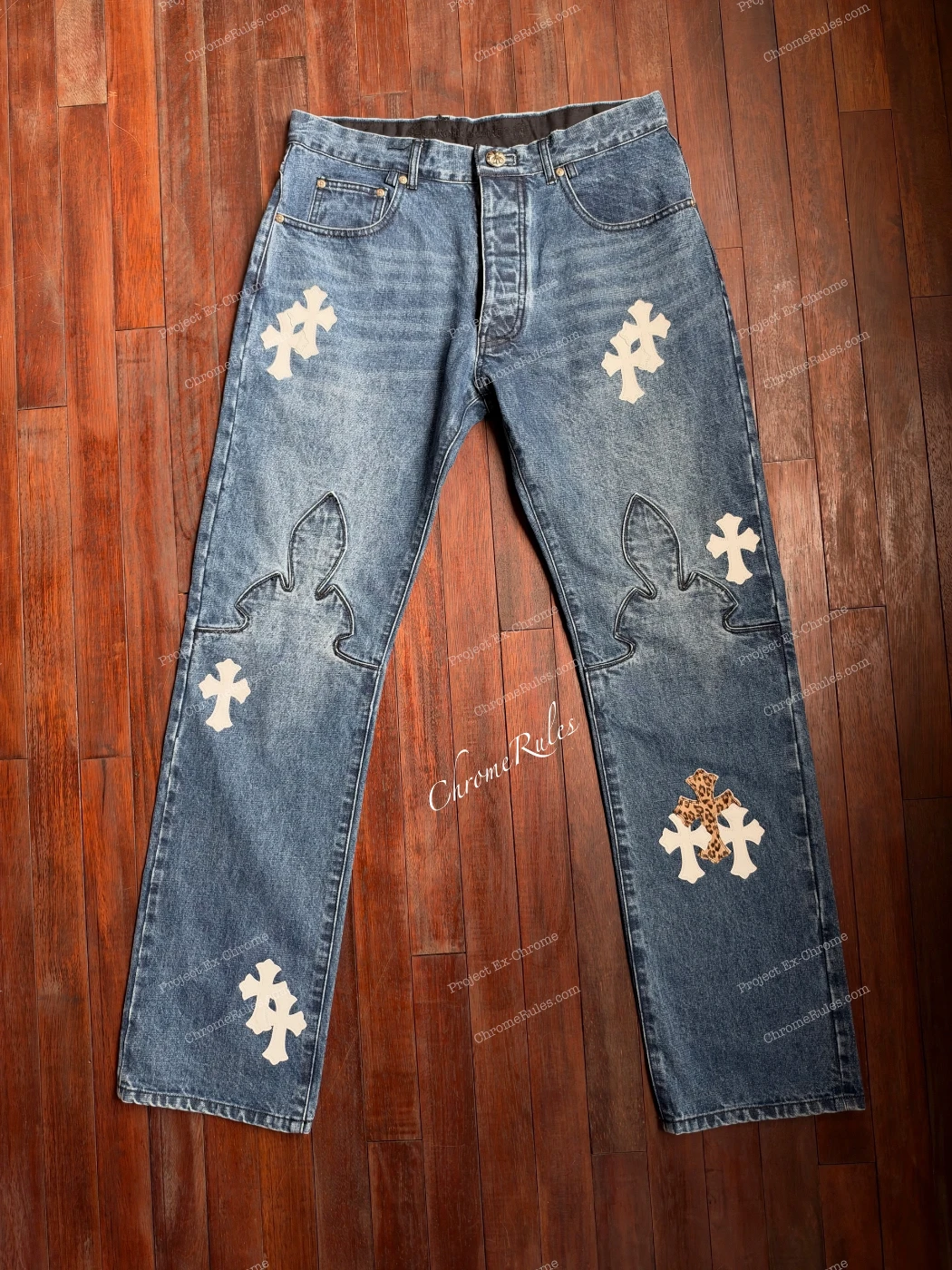 Fleur denim laid flat, with pale cross patches and large outlined motifs at the knees.