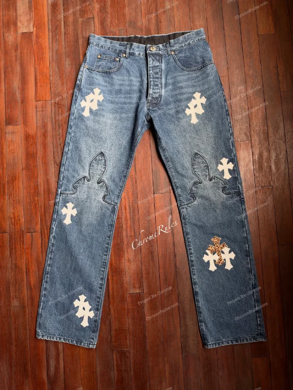 Fleur denim laid flat, with pale cross patches and large outlined motifs at the knees.